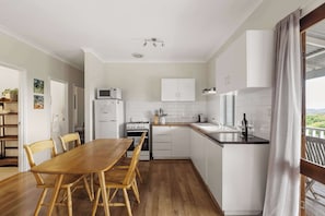 Una cucina moderna con mobili bianchi, un tavolo da pranzo in legno e vista sull'esterno.