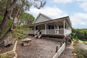 A two-story house with a covered porch, a stone bench, and a wooden fence.