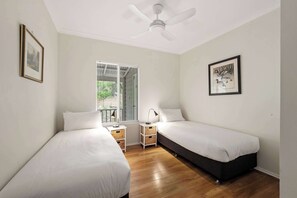 Una camera da letto con due letti, un ventilatore a soffitto, una finestra con persiane e quadri appesi alle pareti.