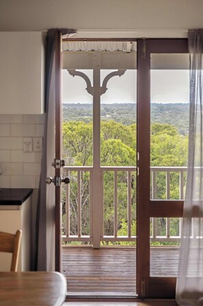 Eine offene Tür, die auf einen Balkon mit Blick auf eine bewaldete Landschaft führt.