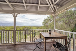 A covered outdoor area with a wooden table and chairs, a bottle, and wine glasses.