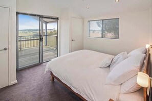 Ein Schlafzimmer mit einem großen Bett, einem Fenster mit Jalousien, einer Balkontür und Blick ins Freie.