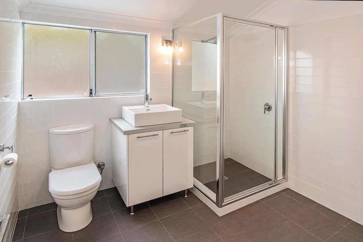 Une salle de bain moderne équipée de toilettes, d’un lavabo, d’un meuble et d’une douche à parois de verre.