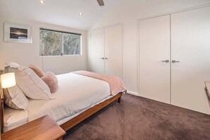 A bedroom with a bed, bedside table, lamp, window, and wardrobe.