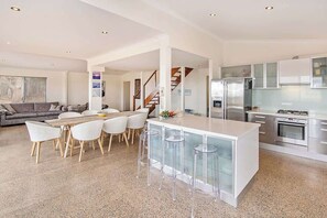 A modern kitchen with a central island, bar stools, and a dining area with a sofa and chairs. - Margaret River Farmhouse: Serene Bushland Getaway (Rosa Glen)