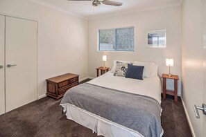 A bedroom with a bed, two bedside tables, a nightstand, a ceiling fan, a window with blinds, and a door. - Margaret River Farmhouse: Serene Bushland Getaway (Rosa Glen)