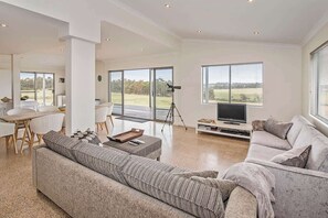 A spacious living area with a large sofa, a dining table, and a TV. - Margaret River Farmhouse: Serene Bushland Getaway (Rosa Glen)