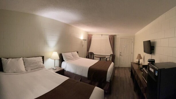 A hotel room with two beds, a TV, a desk, and a fire extinguisher. - Paddock Inn (Coleman)