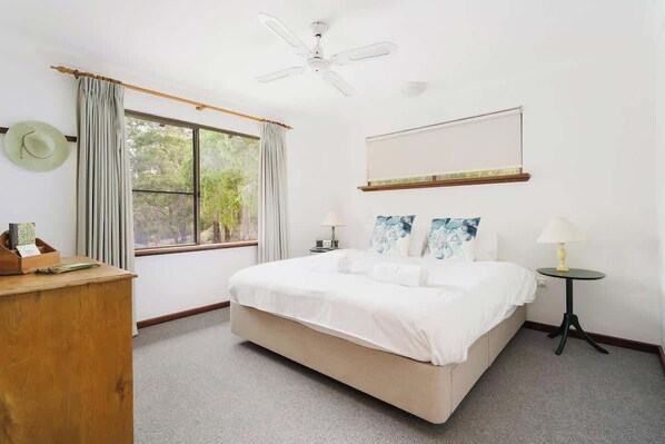 A hotel room with a bed, a desk, a standing lamp, a ceiling fan, and a window with curtains.