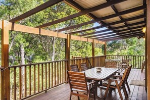 A covered outdoor deck with wooden furniture and a view of trees.