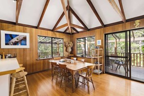 A wooden interior with a dining table, chairs, and large windows.