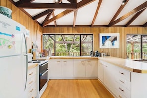 Una cocina con vigas de madera, armarios blancos, un refrigerador y una ventana con vista a follaje.