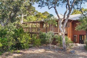 Una baita di legno con veranda, circondata da alberi e un paesaggio arido.
