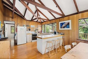 A spacious kitchen with wooden beams, a large island with stools, and a view of greenery outside.