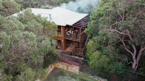 A two-story wooden house with a balcony, surrounded by trees.