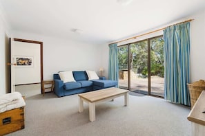 A room with a blue sofa, a wooden coffee table, a wicker basket, and a sliding glass door leading to an outdoor area.