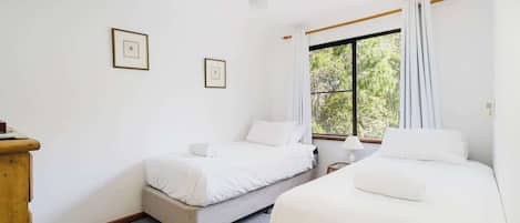 Une chambre avec deux lits, un ventilateur de plafond, une fenêtre avec des rideaux et des tableaux encadrés accrochés au mur.
