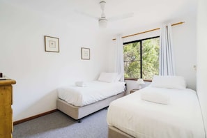 Una camera da letto con due letti, un ventilatore a soffitto, una finestra con tende e quadri appesi al muro.