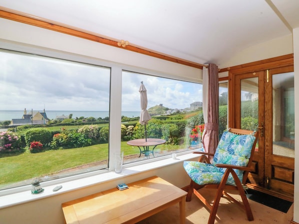 A room with a large window, a wooden bench, a chair with a floral cushion, and a small table.