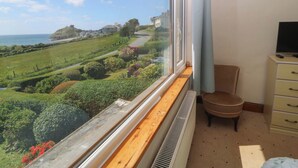 Una habitación con vistas a un paisaje costero, un radiador, una silla y un televisor sobre un aparador.