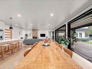 A modern kitchen with a central island, a dining area with a wooden table, and large windows offering a view of the outdoors.