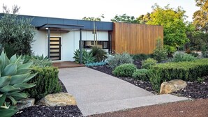 A modern house with a concrete pathway leading to the entrance, surrounded by landscaped gardens and various plants. - Seaview Yallingup—Nature & Spa Sanctuary (Yallingup)