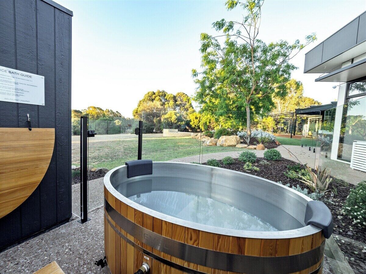 Un jacuzzi con revestimiento de madera, rodeado por un jardín ajardinado con árboles y arbustos.
