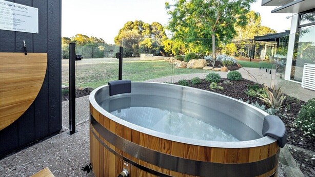 A hot tub with a wooden exterior, surrounded by a landscaped garden with trees and shrubs. - Seaview Yallingup—Nature & Spa Sanctuary (Yallingup)
