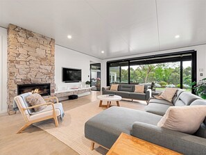 A modern living room with a stone fireplace, a grey sofa, a wooden chair, and a round coffee table. - Seaview Yallingup—Nature & Spa Sanctuary (Yallingup)