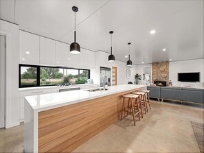 A modern kitchen with a large island, bar stools, pendant lighting, and a stone fireplace. - Seaview Yallingup (Yallingup)