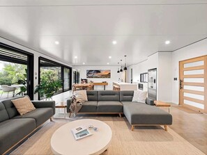 A modern living room with a sectional sofa, a round coffee table, and a dining area with a kitchen in the background.
