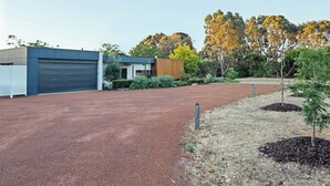 A modern building with a garage, a small wooden structure, and landscaped areas with trees and shrubs. - Seaview Yallingup—Nature & Spa Sanctuary (Yallingup)