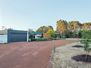 A modern building with a garage, a small wooden structure, and landscaped areas with trees and shrubs. - Seaview Yallingup—Nature & Spa Sanctuary (Yallingup)