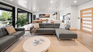 A modern living room with a sectional sofa, a coffee table, and a dining area with a kitchen in the background. - Seaview Yallingup—Nature & Spa Sanctuary (Yallingup)