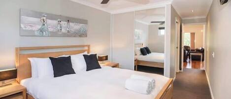 A hotel room with a bed, a ceiling fan, a painting, and a mirror.