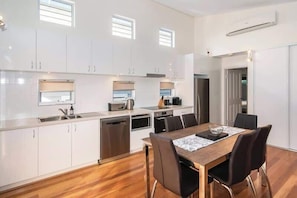 A modern kitchen with white cabinets, a wooden dining table, and a built-in oven. - Villa on the Cape (Dunsborough)