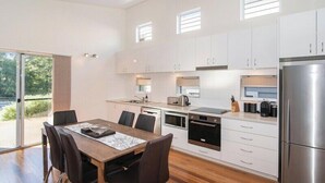 A modern kitchen with a dining area, featuring a stainless steel refrigerator, a built-in oven, and a large window providing natural light. - Villa on the Cape: Relaxed Hideaway near Town (Dunsborough)