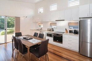 A modern kitchen with a dining area, featuring a stainless steel refrigerator, a built-in oven, and a large window providing natural light. - Villa on the Cape: Relaxed Hideaway near Town (Dunsborough)