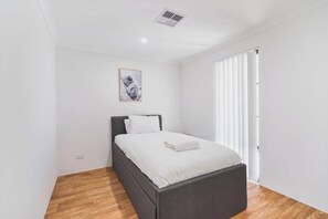 A bedroom with a bed, a picture on the wall, and a window with blinds.