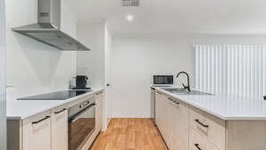A modern kitchen with white cabinetry, a stainless steel range hood, a microwave, and a sink.