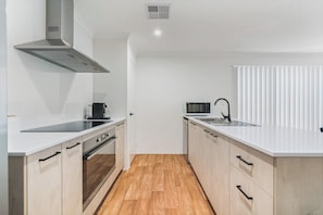 A modern kitchen with white cabinetry, a stainless steel range hood, a microwave, and a sink.