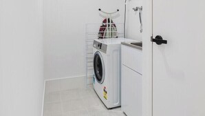 A compact laundry room with a washing machine, a drying rack, and a shower.