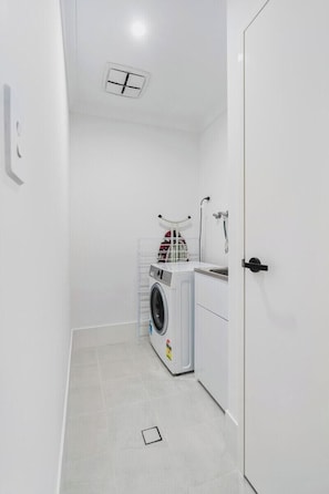 A compact laundry room with a washing machine, a drying rack, and a shower.