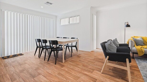 A modern living room with a dining area, featuring a wooden floor, a sofa with cushions, a black armchair, and a table with chairs.