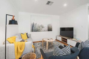 Ein modernes Wohnzimmer mit Sofa, Sessel, Fernseher und Kunstwerk an der Wand.