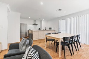 Une cuisine moderne avec un îlot central, un coin repas comprenant une table et des chaises, et un canapé agrémenté de coussins à motifs.