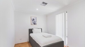 A bedroom with a bed, a picture on the wall, and a window with blinds.