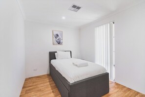 A bedroom with a bed, a picture on the wall, and a window with blinds.