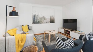 A modern living room with a sofa, armchairs, a TV, and a painting on the wall.