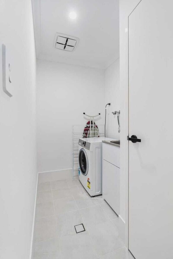 A compact laundry room with a washing machine, a drying rack, and a small sink.